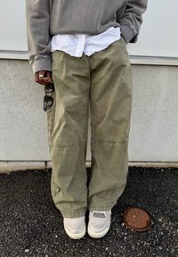 Løse olivengrønne bukser med strukturert finish, kombinert med en grå genser og en hvit skjorte. Grå joggesko med mesh-detalj.