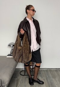 Veste en cuir marron sur une chemise à rayures roses, jupe à fines rayures noires, collants noirs transparents et sac en fourrure brun ébouriffé. Lunettes de soleil noires et chaussures noires.