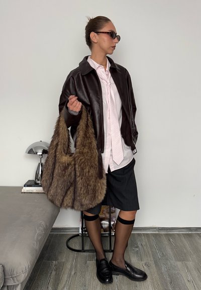 Chaqueta de cuero marrón sobre una camisa a rayas rosa, falda negra a rayas, medias negras transparentes y un bolso de piel marrón de pelo desordenado. Gafas de sol oscuras y zapatos negros.