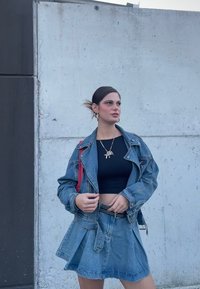 Denim jakna z oversized krojem in svetlim pranjem, v kombinaciji s črnimi krojenimi majicami in denim krilom. Omeniti velja srebrno verižico.
