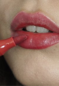 Rode lipcrayon aangebracht op volle lippen, die de roze en rode tinten verbetert. De lippen zijn glad met een glanzende afwerking en subtiele textuurvariaties.