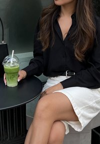 Μαύρο πουκάμισο με κουμπιά, λευκή φούστα και ένα πράσινο ποτό σε πλαστικό ποτήρι με καλαμάκι σε στρογγυλό μαύρο τραπέζι, δημιουργώντας μια χαλαρή σκηνή φαγητού.