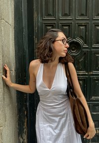 Biela holá šaty s hlbokým výstrihom do V, skombinované s hnedou semišovou kabelkou cez rameno. Pozadie zdobí textúrované zelené dvere.