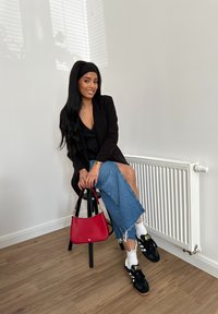 Sort blazer over en sort top, parret med en denimnederdel. Rød håndtaske, hvide sokker og sorte sneakers. Minimalistisk indendørs indstilling.