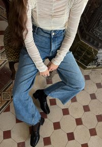 Haut en long manches léger et texturé associé à un jean bleu ample taille haute et des mocassins noirs, présentant des détails soignés et des ourlets effilochés.