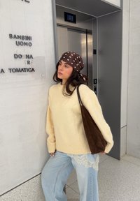 Kreemjas kampsun soonikkoes äärega, sinised laia säärega teksad pitsdetailiga ja pruun-mustriline peapael, kandmas tumepruuni seemisnahast kotti.