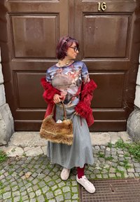 Hosszú ujjú grafikás póló élénk képekkel, piros műszőrme kabát, kockás szoknya, barna szőrös táska, rózsaszín fűzős sportcipő, összefonódó macskakövek.