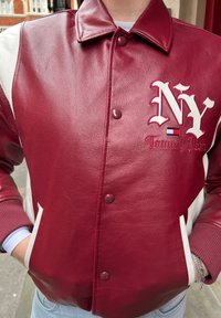 Giubbotto bomber in pelle rossa con accenti bianchi, chiusura a bottoni e ricamo 'NY'. Collo arrotondato e polsini a costine. Materiale testurizzato.