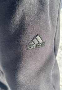 Fekete sportos szövet, textúrált felülettel, a középpontban egy jellegzetes fekete Adidas logóval, három ferde csíkkal.
