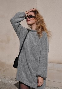 Sivi oversized pulover s dugim rukavima, visokim izrezom i mekim, teksturiranim završetkom. Nosite ga uz malu crnu torbicu i uzorkovane tajice.