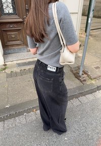 Suéter gris de manga corta combinado con jeans negros de corte holgado que tienen una etiqueta que dice "PNTS". Pequeño bolso beige llevado al hombro.