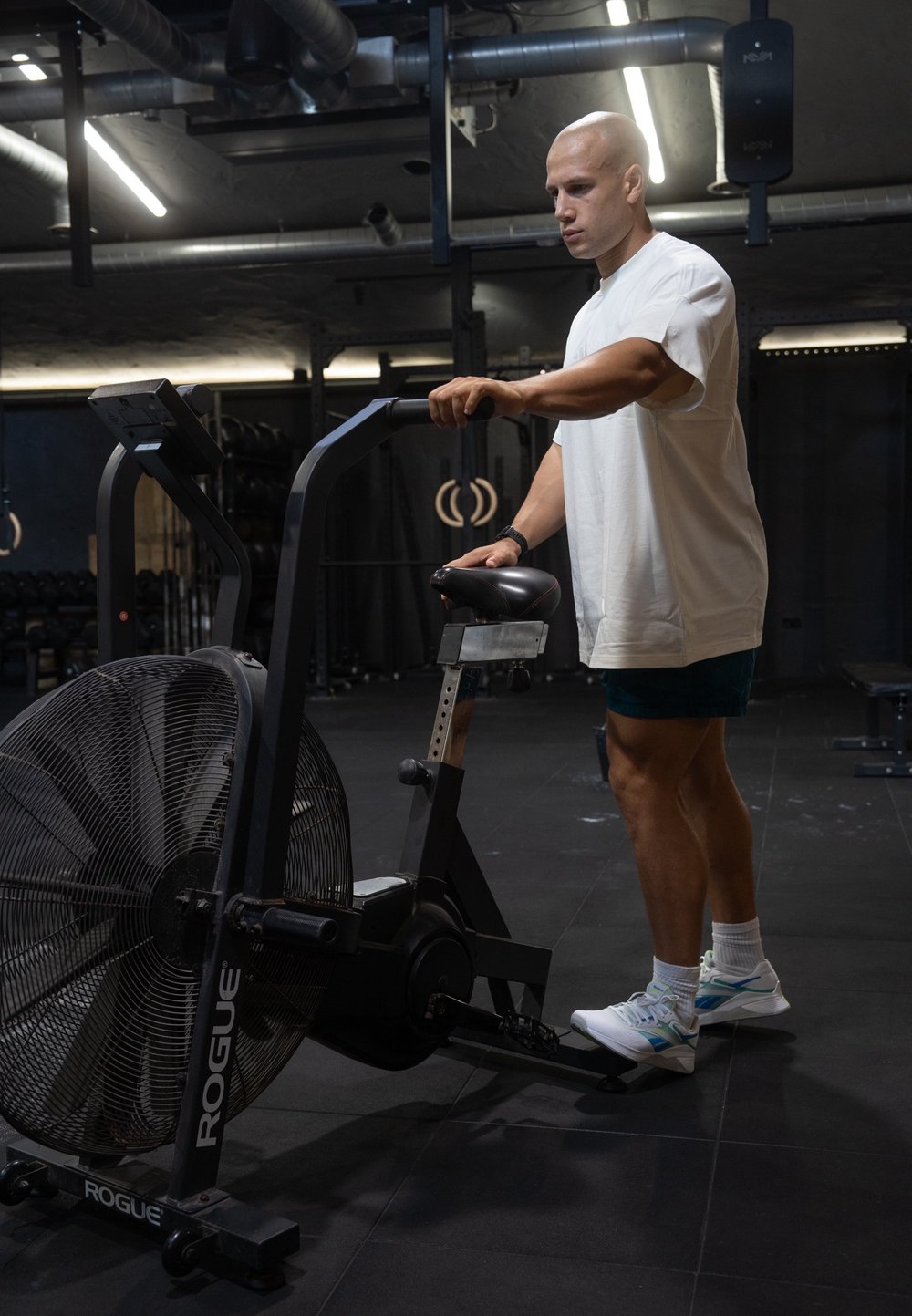 Luftcykel med en stor frontvifte, sort ramme, justerbart sæde og digitalt display. Bruger iført hvid skjorte og blå shorts.