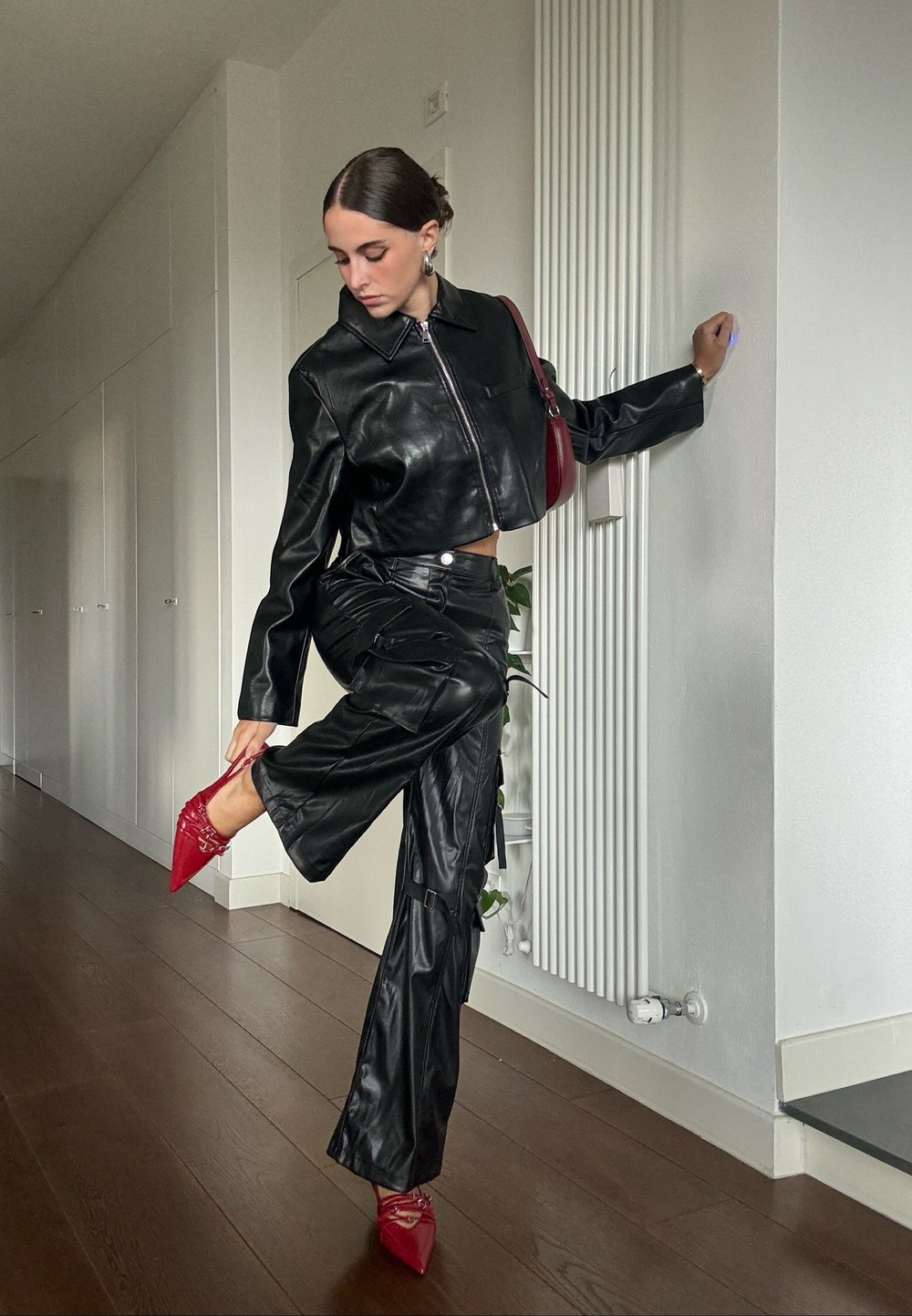 Μαύρο δερμάτινο κοντό μπουφάν με φερμουάρ, συνδυασμένο με μαύρο δερμάτινο cargo παντελόνι. Κόκκινες στιλέτο γόβες τονίζουν το σύνολο.