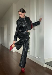 Μαύρο δερμάτινο κοντό μπουφάν με φερμουάρ, συνδυασμένο με μαύρο δερμάτινο cargo παντελόνι. Κόκκινες στιλέτο γόβες τονίζουν το σύνολο.