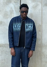 Giubbotto in denim blu scuro con chiusura a zip, caratterizzato da un motivo a pois sfumati e la parola "LEGACY" in azzurro sul davanti.