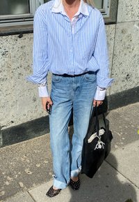 Ριγέ μπλε και λευκό πουκάμισο με κουμπιά, ανοιχτό μπλε τζιν, μαύρη τσά�ντα, και μαύρες μπαλαρίνες με πουά σχέδιο, υφασμάτινη επιφάνεια και διακοσμητικό κρεμαστό.