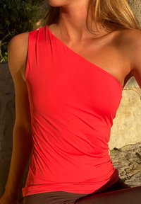 Naisso wearing a erksinine üheõlgne tipp, istub õues, taustal kivid ja rohelus, päike valgustab nahka ja kangast.