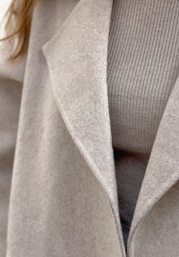 Abrigo de lana beige con solapa sobre un suéter de canalé topo, mostrando capas de texturas y tejidos invernales en tonos neutros.