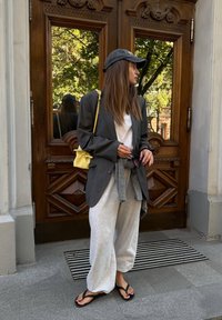 Przesadnie duża szara marynarka założona na białą koszulkę, szare dresy i czarne klapki. Mała żółta torebka na ramię i okulary przeciwsłoneczne w ręku.
