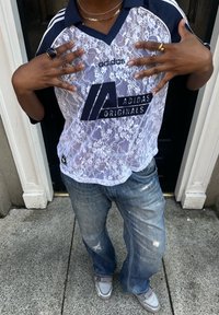 Hvit blonde Adidas jersey med marineblå detaljer og logo, kombinert med slitte denimjeans og grå sneakers, med en avslappet passform.