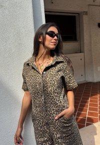 Macacão em padrão de leopardo com mangas curtas, fecho à frente com botões, bolsos laterais e um corte solto. Tecido suave com textura e um padrão ousado.