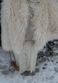 Chaqueta de piel sintética color crema, superpuesta sobre una blusa beige y una falda de encaje, combinada con un bolso marrón claro y zapatos marrones sobre suelo nevado.