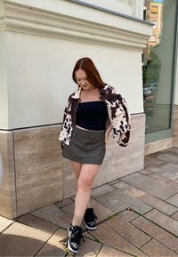 Brun og hvid mønstret jakke, sort strapless top, grå mini nederdel og sorte sneakers med hvide detaljer. Overfladerne er flisebelagte.