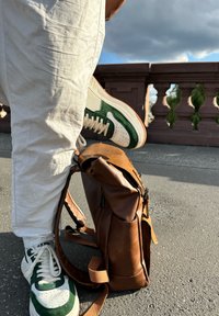 Green and white sneakers with perforated detailing, paired with a brown leather backpack featuring zippers and side pockets.