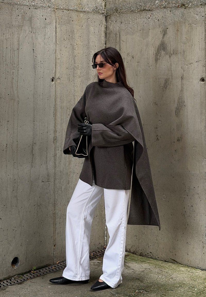 Grey oversized top with dramatic sleeves, paired with white wide-leg trousers and black pointed shoes. Accessories include black gloves and a small bag.
