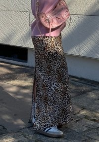Falda maxi de estampado de leopardo con aberturas laterales, fabricada en un tejido ligero. Combinada con un bolso de mano rosa brillante y zapatillas grises.