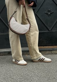 Beige wide-leg jeans, white and brown trainers with three stripes, and a crescent-shaped bag featuring a woven pattern and brown leather accents.