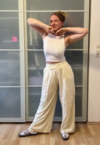 Bílý, žebrovaný crop top a světle žluté pruhované kalhoty širokého střihu. Nohy ve vysoce kontrastních černo-bílých teniskách. Pozadí obsahuje posuvné skleněné dveře.