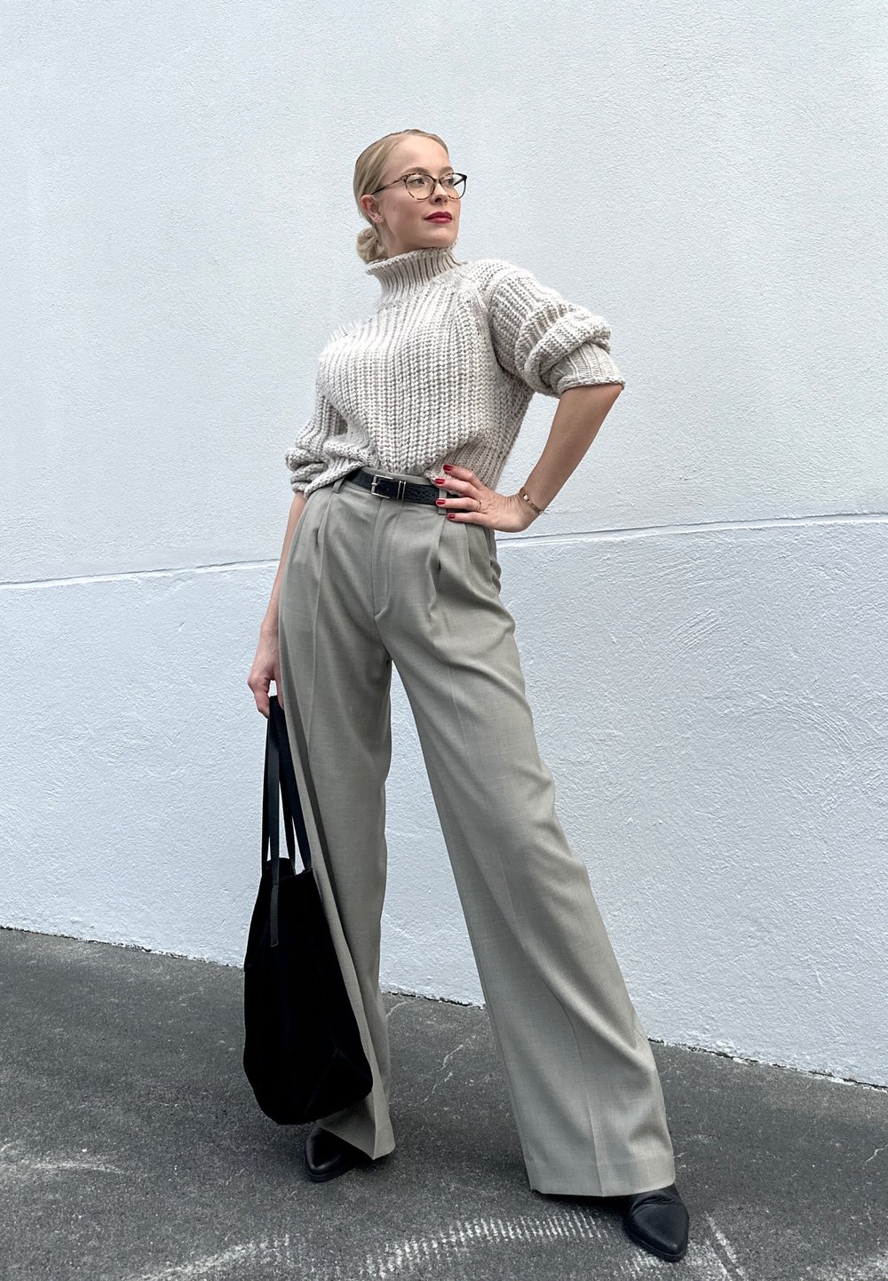 Pleteni krem turtleneck pulover, krojene sive hlače z visokim pasom, črn pas, črna torba, in črne čevlje s peto. Gladka tekstura.