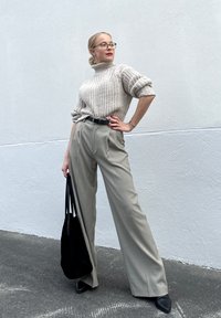 Pleteni krem turtleneck pulover, krojene sive hlače z visokim pasom, črn pas, črna torba, in črne čevlje s peto. Gladka tekstura.