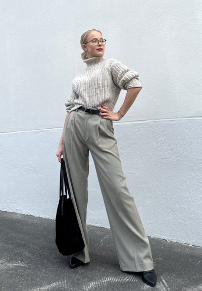 Suéter de punto crema con cuello alto, pantalones grises de talle alto a medida, cinturón negro, bolso tote negro y zapatos negros de tacón. Textura suave.