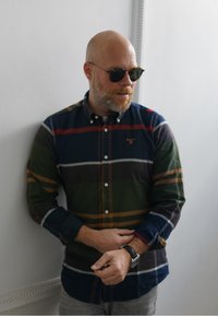 Uma camisa xadrez multicolorida em verde, azul-marinho e bordô, com colarinho abotoado, mangas compridas e um logótipo bordado no peito.