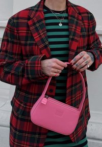 Red and black check blazer worn over a green and black striped dress, holding a small pink leather handbag with a zip and shoulder strap.