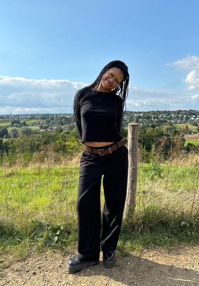 Top negro de manga larga con diseño crop, combinado con pantalones negros holgados y zapatos negros grandes. Entorno al aire libre con vegetación y cielo.