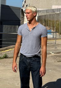 Grå ribbet kortærmet skjorte med knaplukning, parret med mørkeblå denimjeans. Modellen har kort, blegnet hår og står udendørs.
