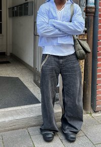 Μπλε ριγέ υπερμεγέθη κοντομάνικο πουκάμισο, φορεμένο πάνω από ένα άσπρο τοπ, σε συνδυασμό με χαλαρά σκούρα τζιν με αλυσίδα και μαύρα παπούτσια.