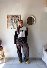 Bela grafična majica s črnimi detajli, oblečena čez prosojeno črno dolgo majico, v kombinaciji z rjavimi hlačami z leopardjim vzorcem in rumenimi čevlji.