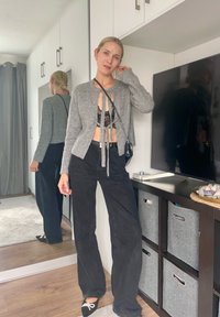 Szürke cropped kardigán egy fekete csipke bralette felett, magas derekú fekete nadrággal párosítva. Fekete cipők fehér masnival, és egy kis táska.