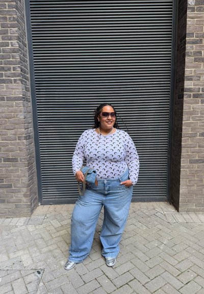 Top gris de manga larga con patrón de luna creciente negra, combinado con vaqueros de pierna ancha azul claro decorados con salpicaduras de pintura blanca. Zapatillas plateadas.