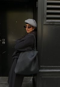 Melna austa somiņa ar teksturētu virsmu, apvienota ar melnu pārmērīgu džemperi un melnbaltu svītrainu bereti.