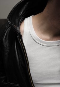 Chaqueta de cuero negra medio desabrochada, revelando una camiseta de tirantes blanca ajustada debajo. Enfoque en la textura y los colores contrastantes.