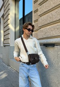 Ανοιχτό μπεζ πλεχτό πουλόβερ, ανοιχτό μπλε τζιν και μια μικρή καφέ δερμάτινη τσάντα χιαστί με καπάκι και λεπτομέρεια αγκράφας.