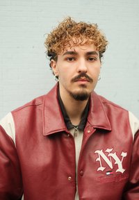 Bordový kožený kabát s krémovými rukávy, s logem "NY" a červenými akcenty. Model má pod ním černé zipové triko.