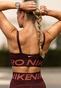 Bordo sportski grudnjak s podesivim trakama i bijelim Nike logotipom; u paru s odgovarajućim visokim tajicama koje imaju istaknuti brend.