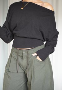 Schwarzer Schulterfreier Pullover mit geripptem Saum, kombiniert mit lockeren olivgrünen Hosen mit Kordelzug und Seitentaschen.