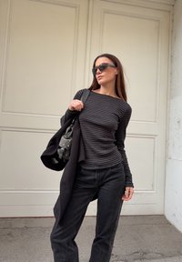 Black long-sleeve striped top paired with high-waisted black jeans. Grey studded bag. The model is standing against a white wall.